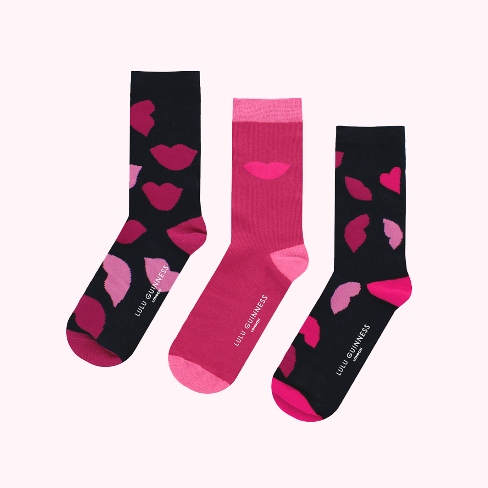 Three pairs of Lulu Guinness socks with pink lips print on a dark and pink background.
