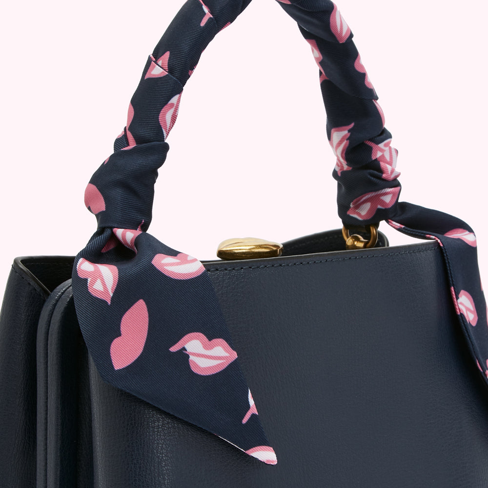 Close-up of a navy blue handbag with a pink lips patterned scarf handle.
