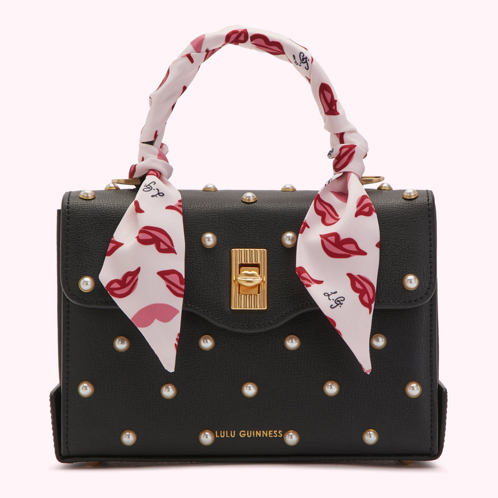 Black Lulu Guinness handbag with pearl accents and a pink lip-print scarf handle.
