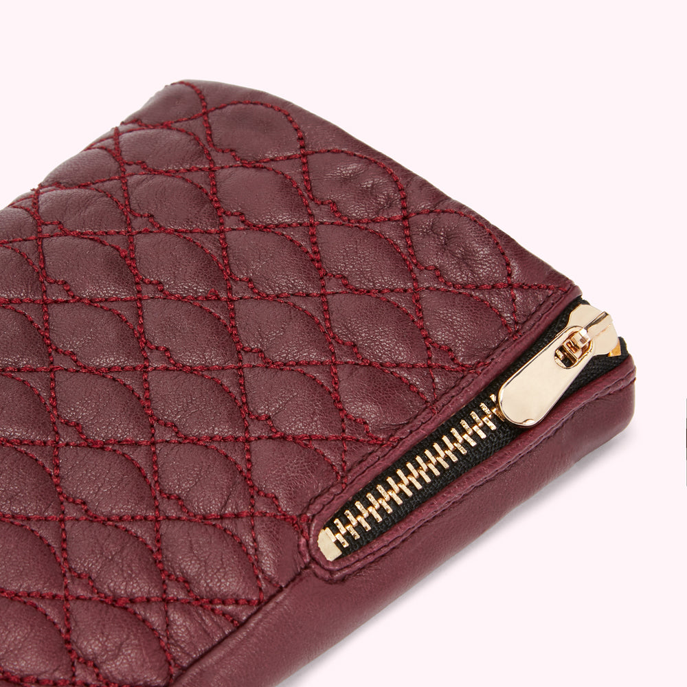 Close-up of a burgundy quilted leather wallet with a gold zipper.
