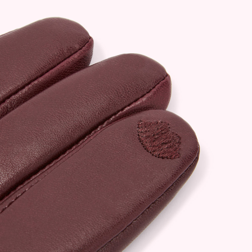 Close-up of burgundy leather gloves with a small embroidered heart detail.

