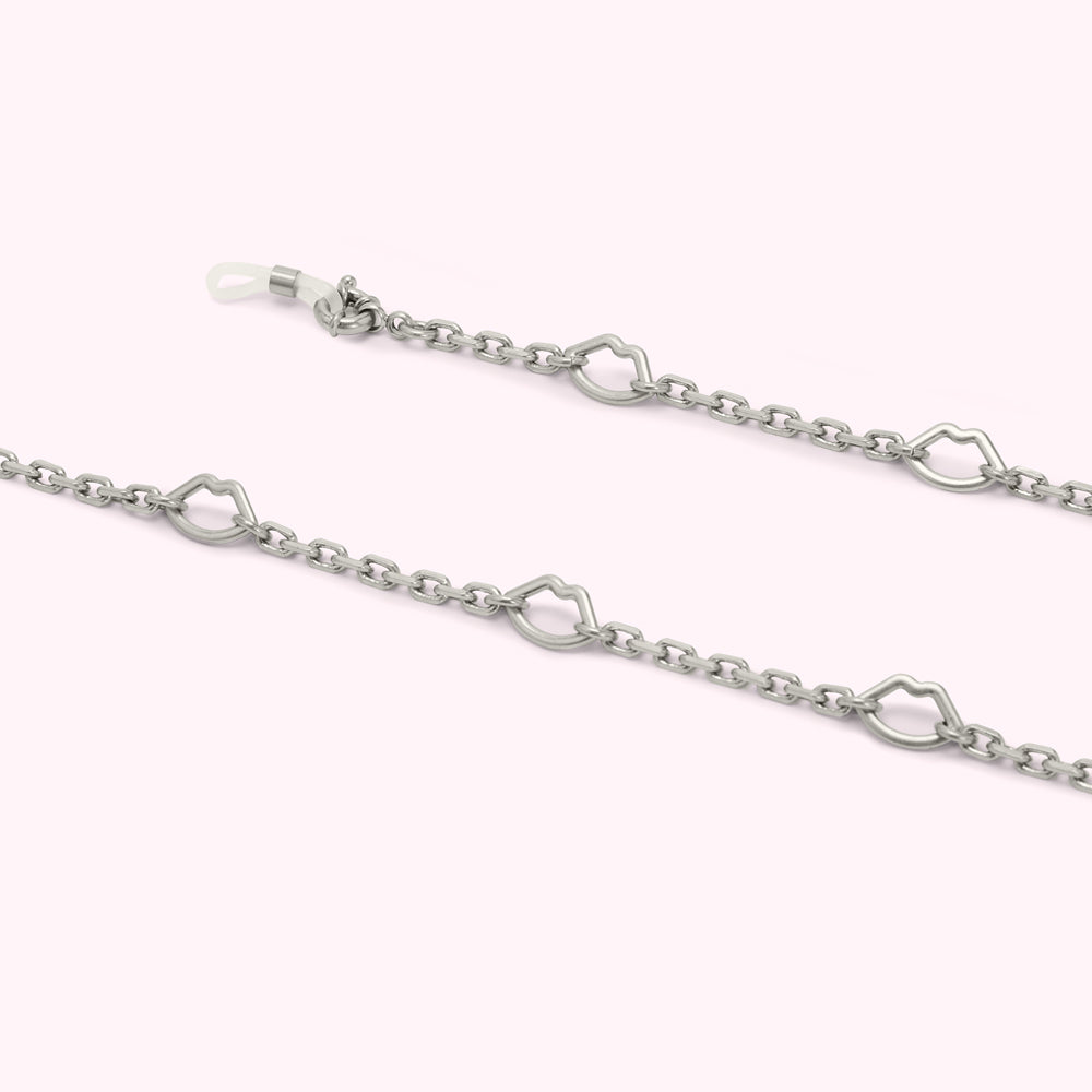 Silver eyeglasses chain with lip-shaped links against a light pink background.
