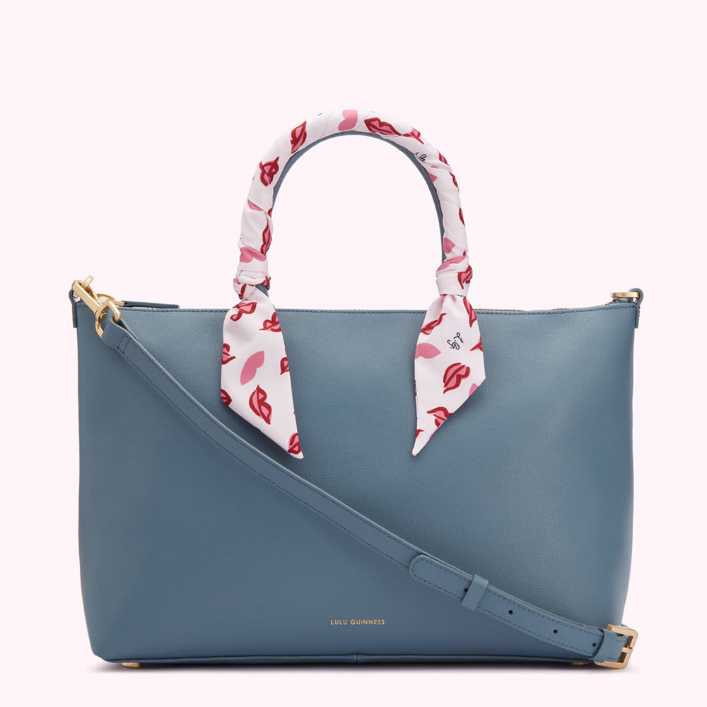 A blue Lulu Guinness tote bag with a white scarf adorned with red lips printed on it.