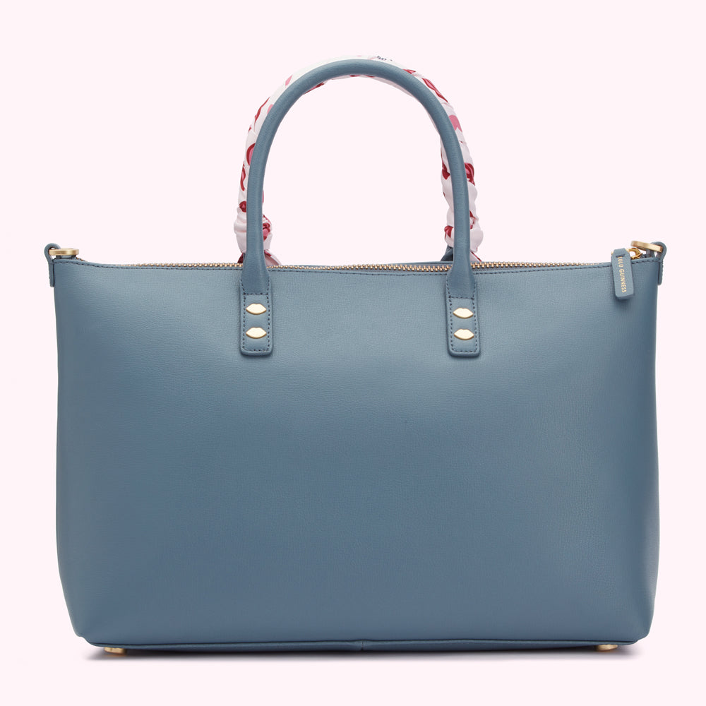 A dusty blue leather tote bag with gold hardware and a silk scarf detail on the handles.
