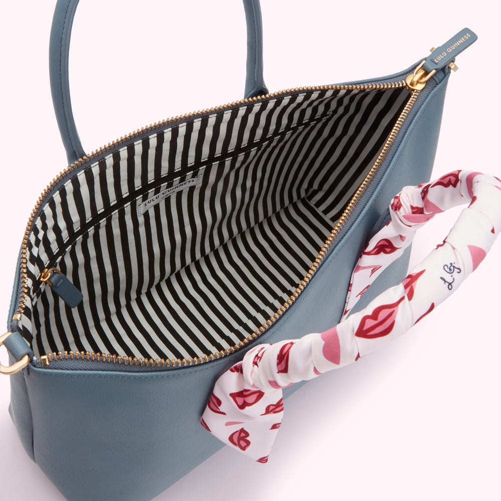 Interior of a Lulu Guinness blue satchel handbag with black and white striped lining and pink lips patterned handle.