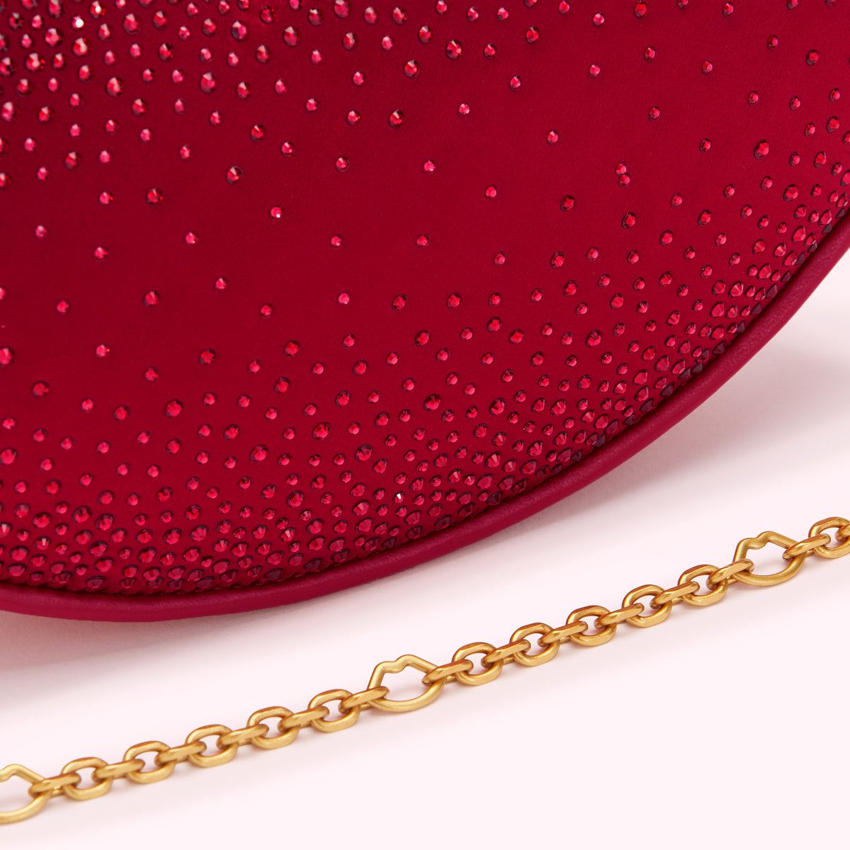 Close-up of a crimson red handbag with red crystal embellishments and a gold chain strap.