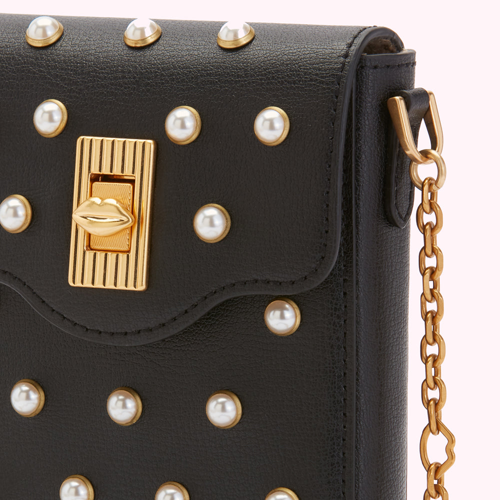 Close-up of a black leather crossbody bag adorned with pearl accents and a gold lip-shaped clasp.
