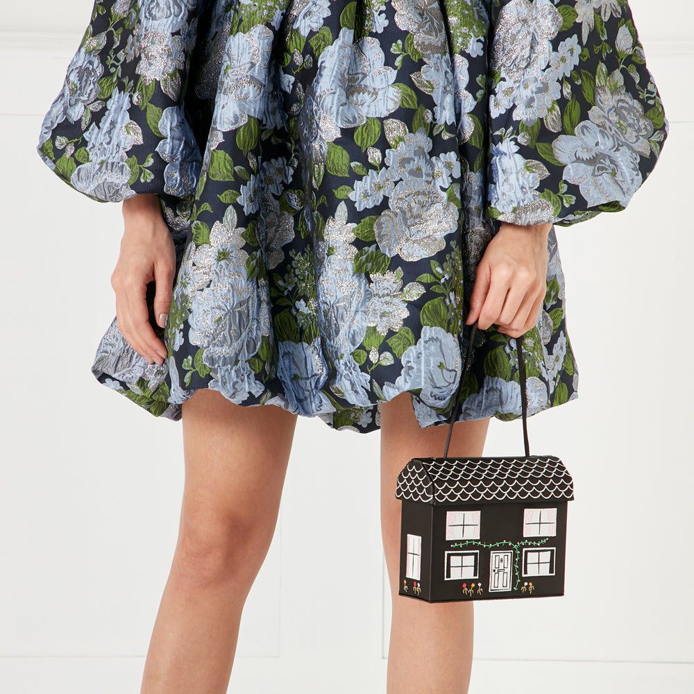 Woman in blue floral dress holding a black house-shaped purse.
