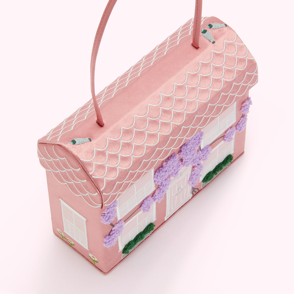 Pink house-shaped handbag with embroidered details.