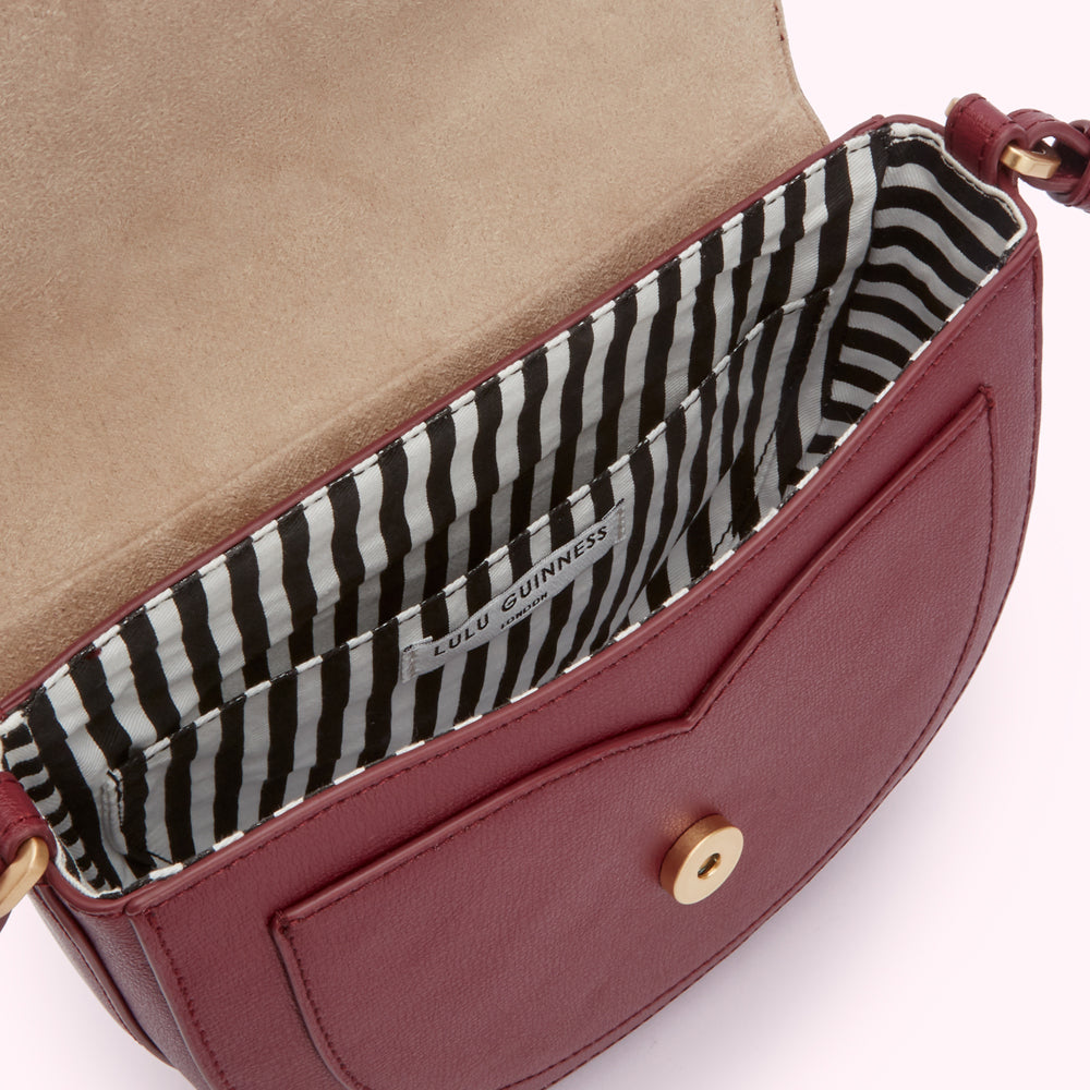 Inside of a burgundy Lulu Guinness crossbody bag showing black and white striped lining and gold-toned clasp.