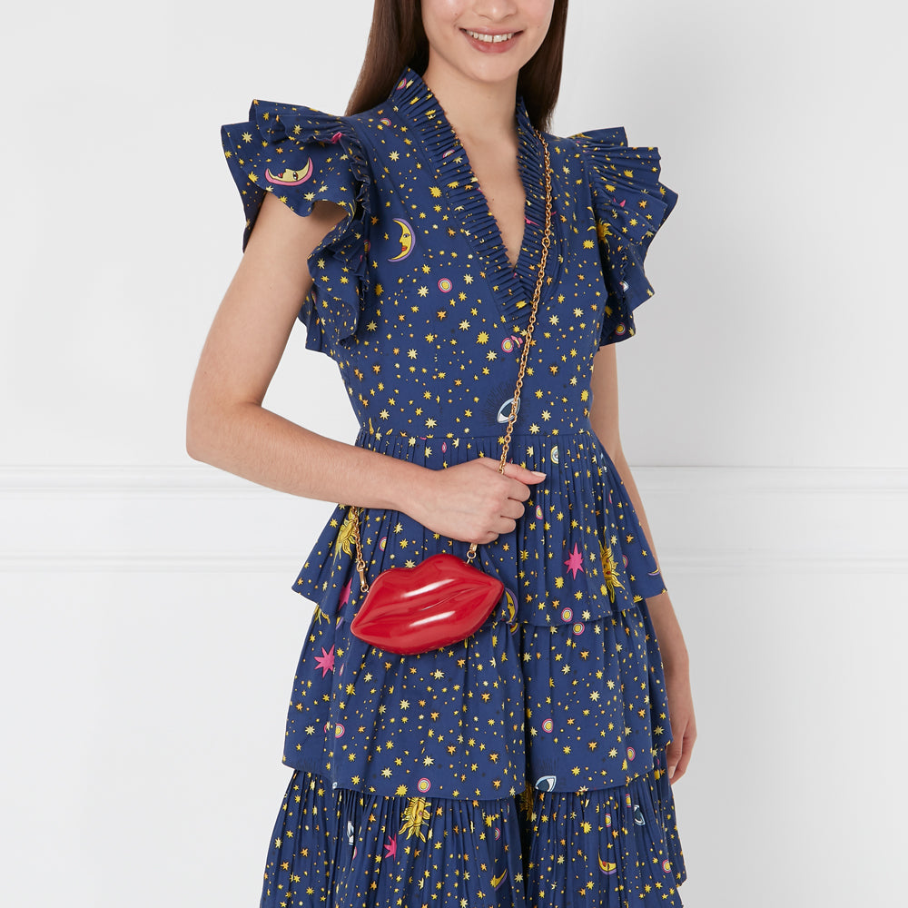 Woman in a navy blue dress with stars and celestial bodies print holding a red lips-shaped crossbody bag.