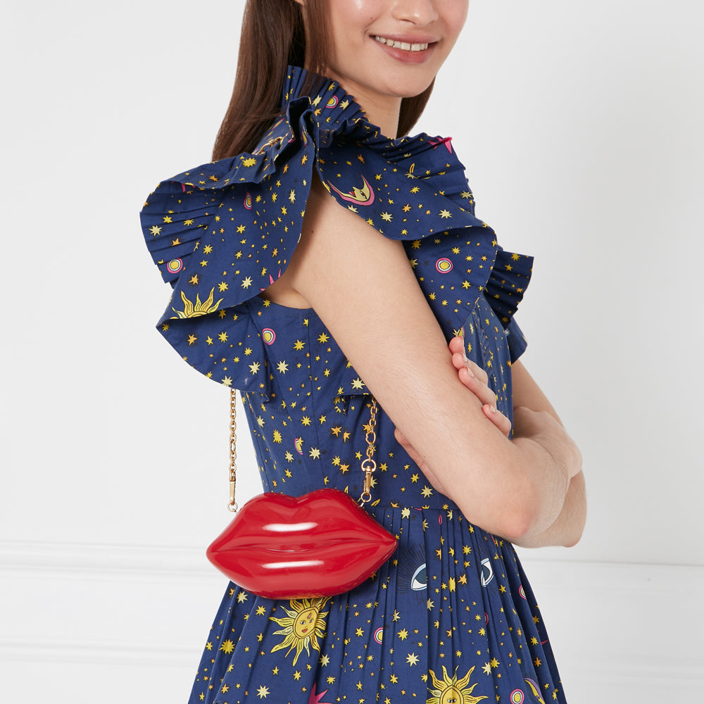 Woman in a blue star print dress holding a red lip-shaped clutch purse with a gold chain.