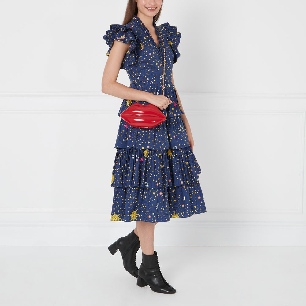 Woman in a blue star print dress holding a red lip-shaped purse.
