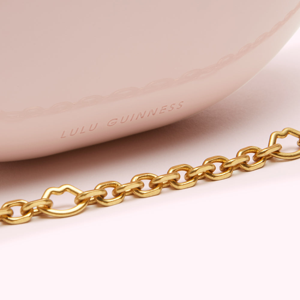 Close-up of a blush pink Lulu Guinness bag with a gold chain strap.