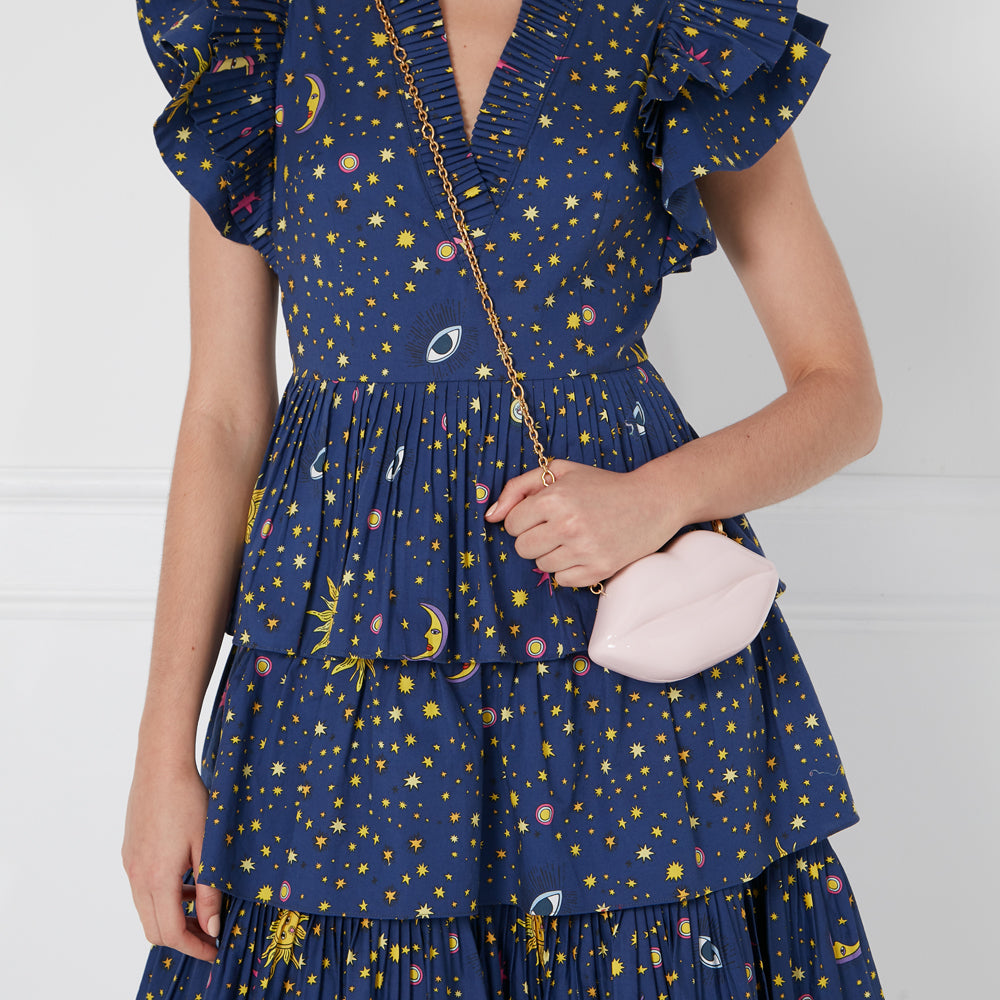 Woman in a blue celestial print dress holding a pink lip-shaped crossbody bag.
