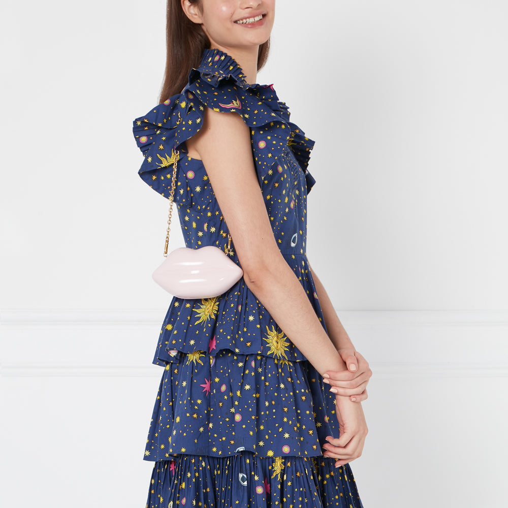 A woman in a navy blue dress with a celestial print carries a pale pink lip-shaped handbag.