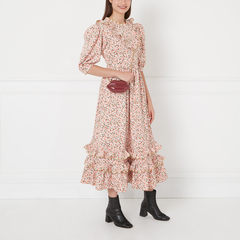 A model wears a pink floral midi dress with ruffles and black ankle boots; she carries a dark-red lip-shaped purse.