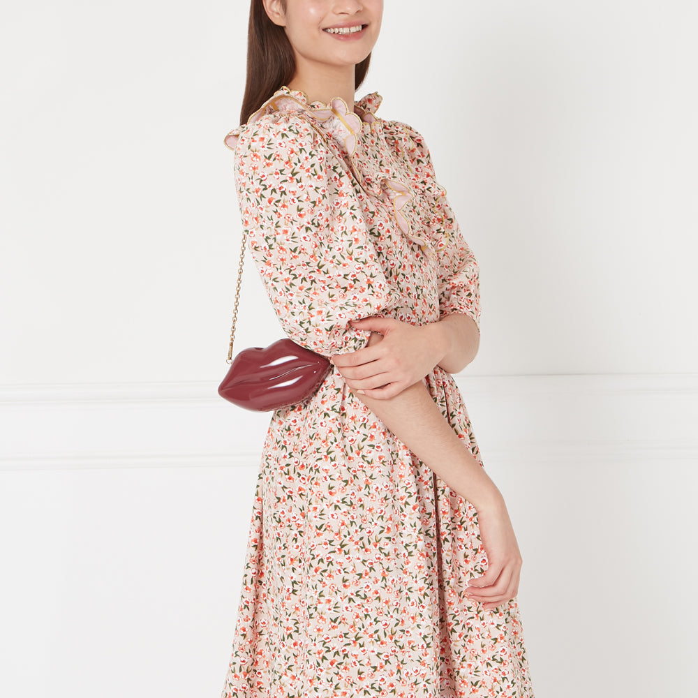 Woman in floral dress holding a burgundy lip-shaped crossbody bag.
