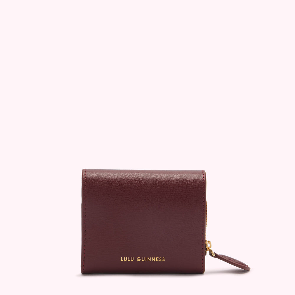 Burgundy Lulu Guinness zip-around wallet on white background.
