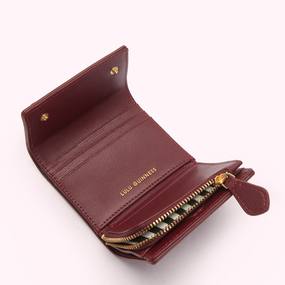 Open burgundy Lulu Guinness wallet with gold zipper and accents against a white background.
