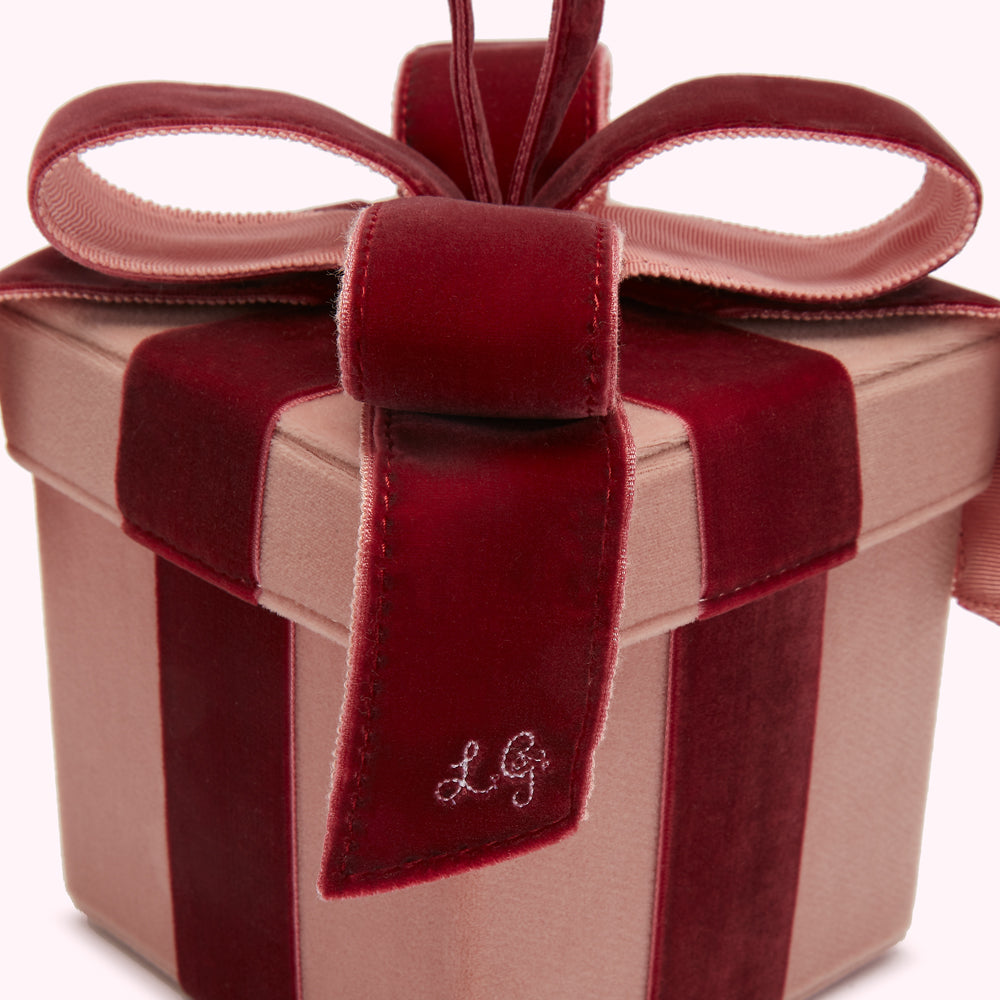 Close-up of a blush pink velvet gift box with a burgundy velvet ribbon and bow, the initials "LG" embroidered on the ribbon.
