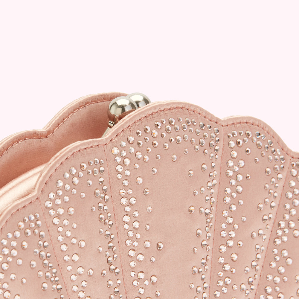 Close-up of a blush pink, seashell-shaped clutch embellished with crystals.

