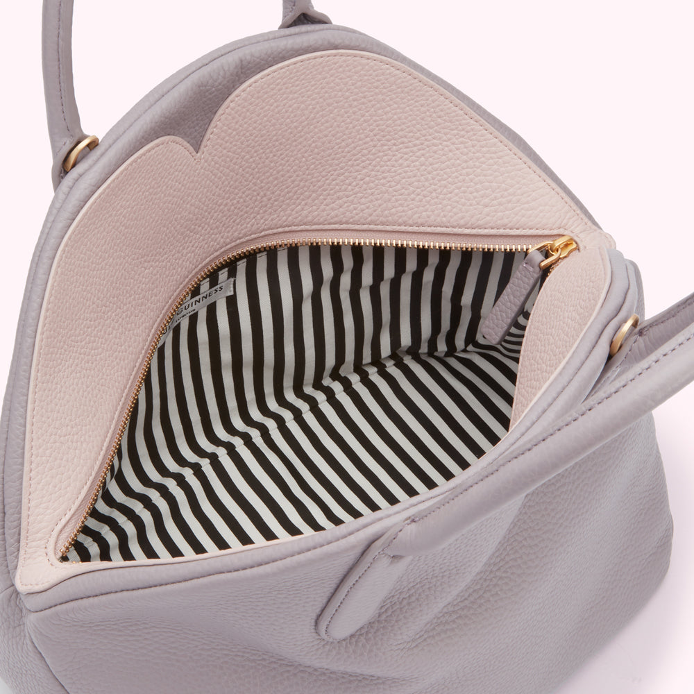 A dusty purple leather handbag with a pale pink interior and black and white striped lining is open, showcasing its details.
