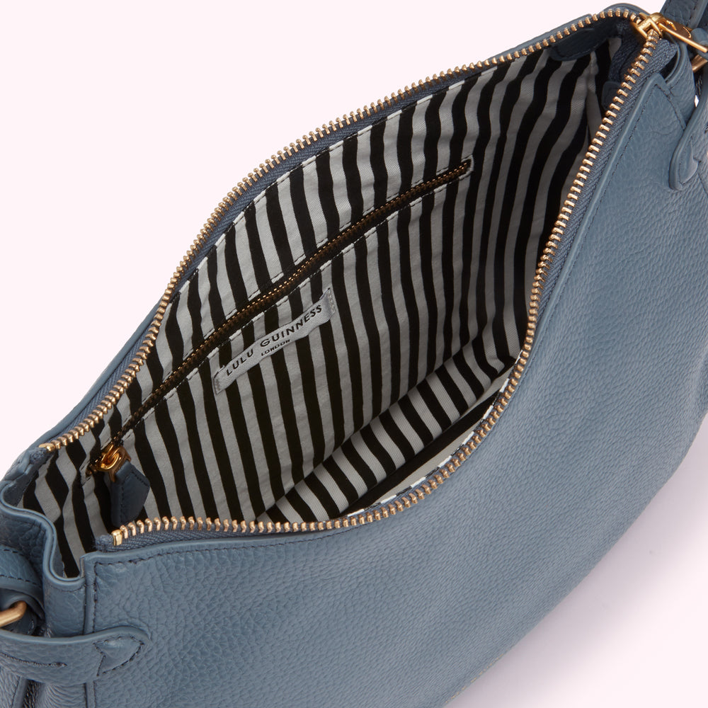 Inside of a blue Lulu Guinness crossbody bag with a black and white striped lining.