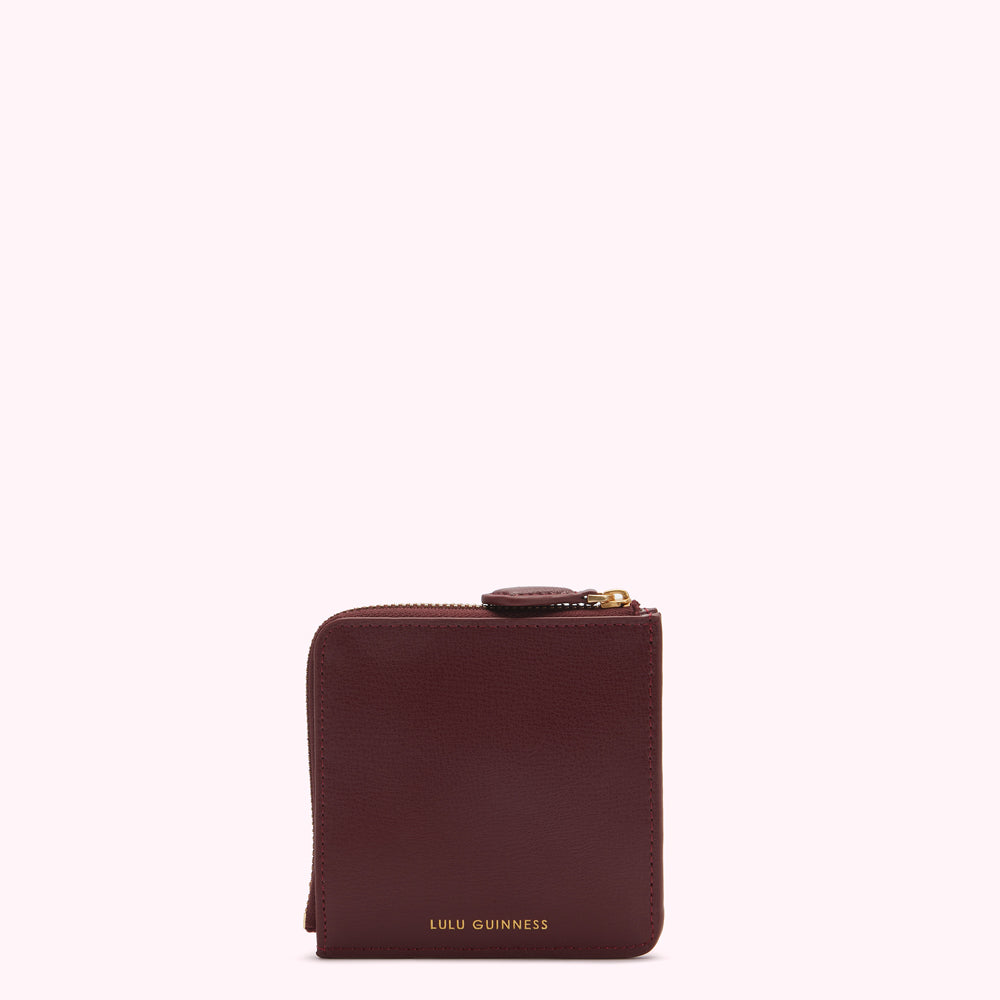 A burgundy Lulu Guinness zip-around wallet against a white background.
