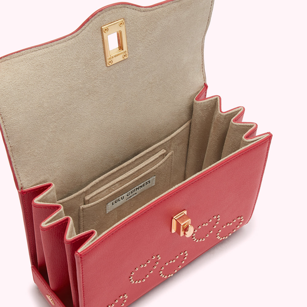 Red Lulu Guinness handbag open to reveal beige interior with studded detail.