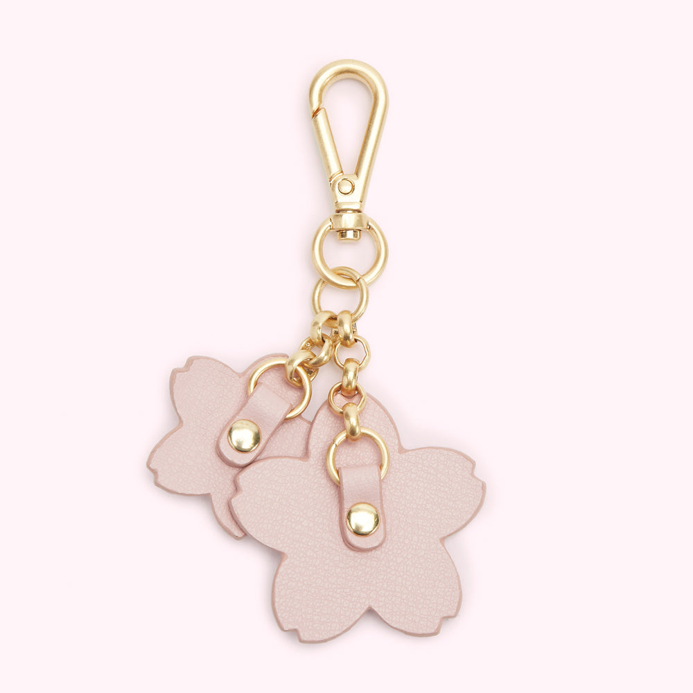 Pink leather cherry blossom keychain with gold hardware against a light pink background.
