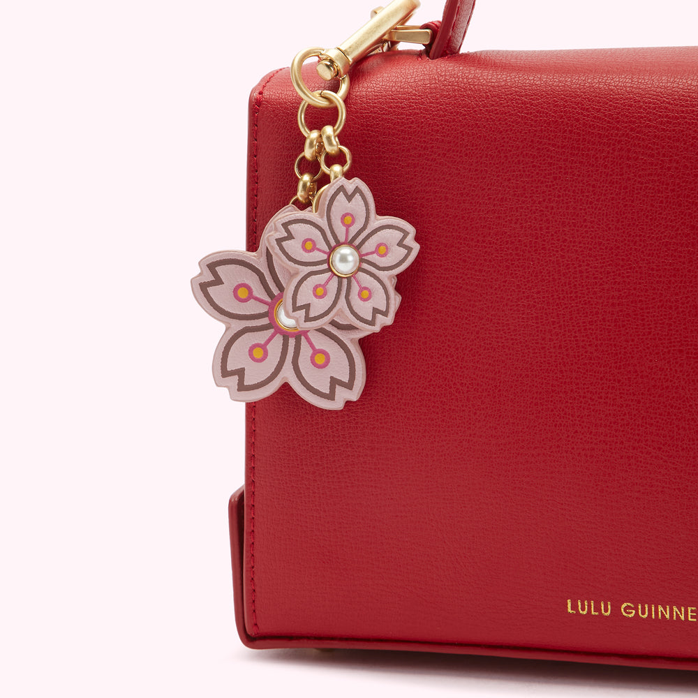 Close-up of a red Lulu Guinness handbag with a pink cherry blossom charm attached.
