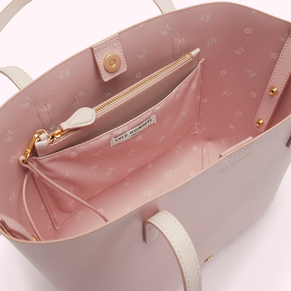 Interior view of a blush pink Lulu Guinness tote bag with a small internal zipped pocket; the bag lining features a repeating pattern of the Lulu Guinness logo and small flowers.
