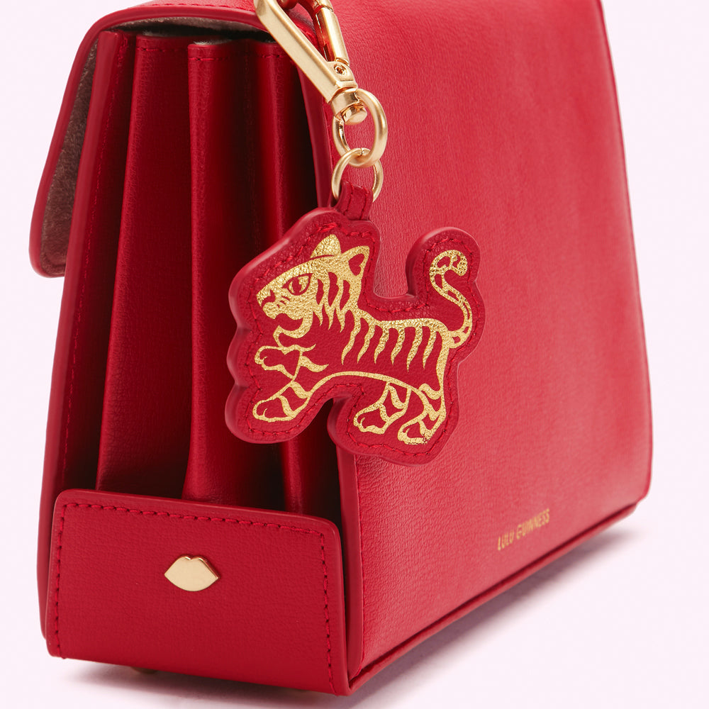 Close-up of a red leather handbag with a gold tiger charm.
