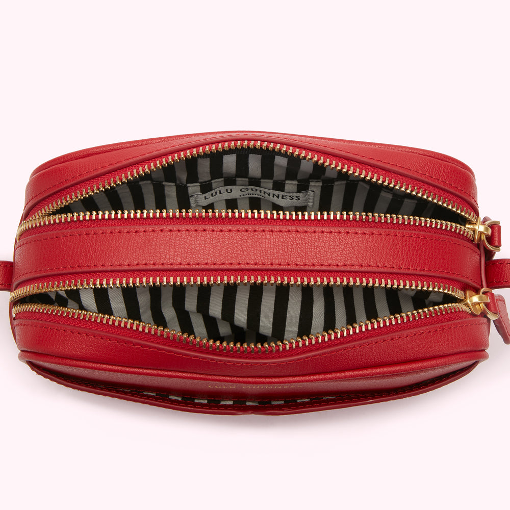 Red Lulu Guinness crossbody bag open to show black and white striped interior.
