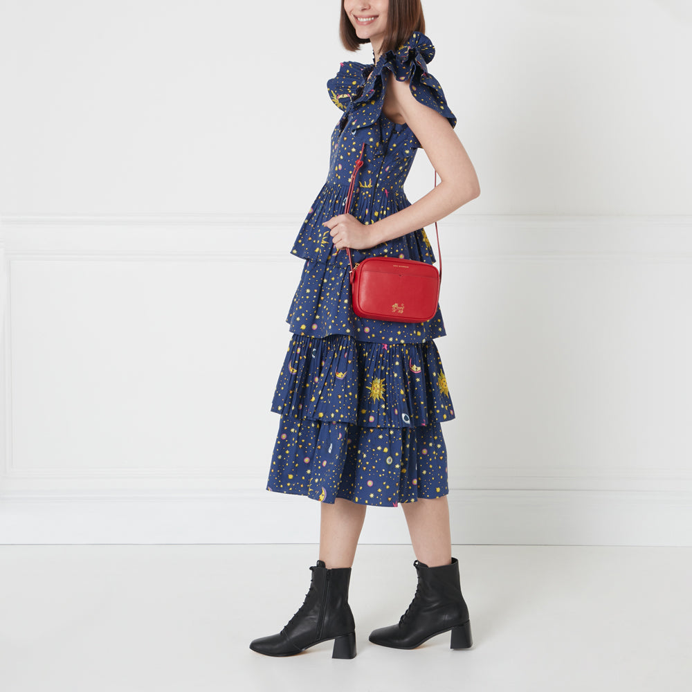 A woman in a blue dress with a celestial print carries a red crossbody bag.
