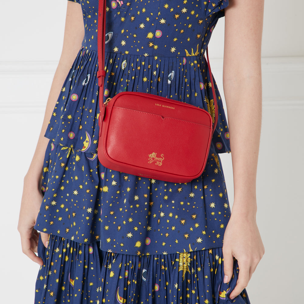 Red Lulu Guinness crossbody bag with gold tiger emblem on a navy dress with celestial print.
