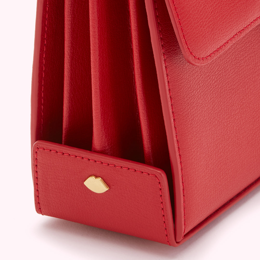 Close-up of a red leather handbag's bottom, showcasing the stitching and a gold lip-shaped logo.

