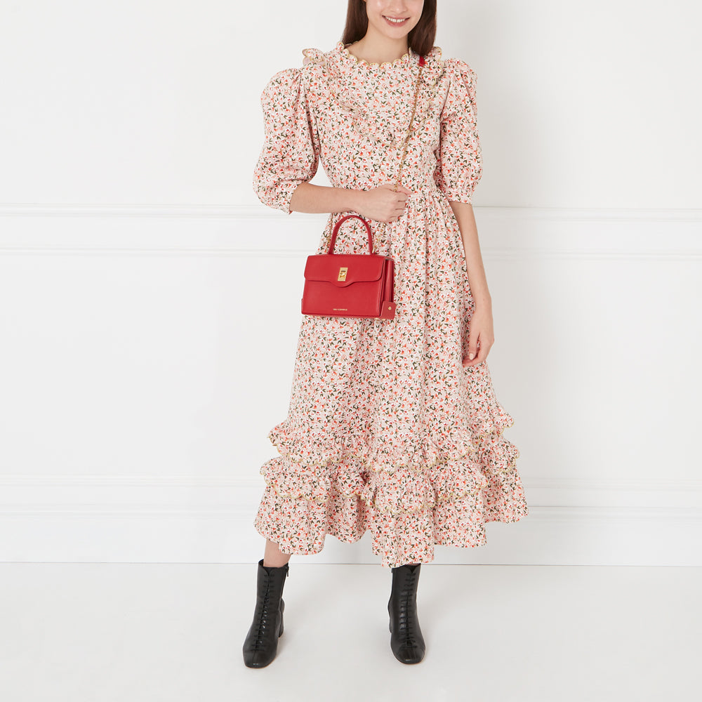 Woman in floral dress and black boots holding a red handbag.
