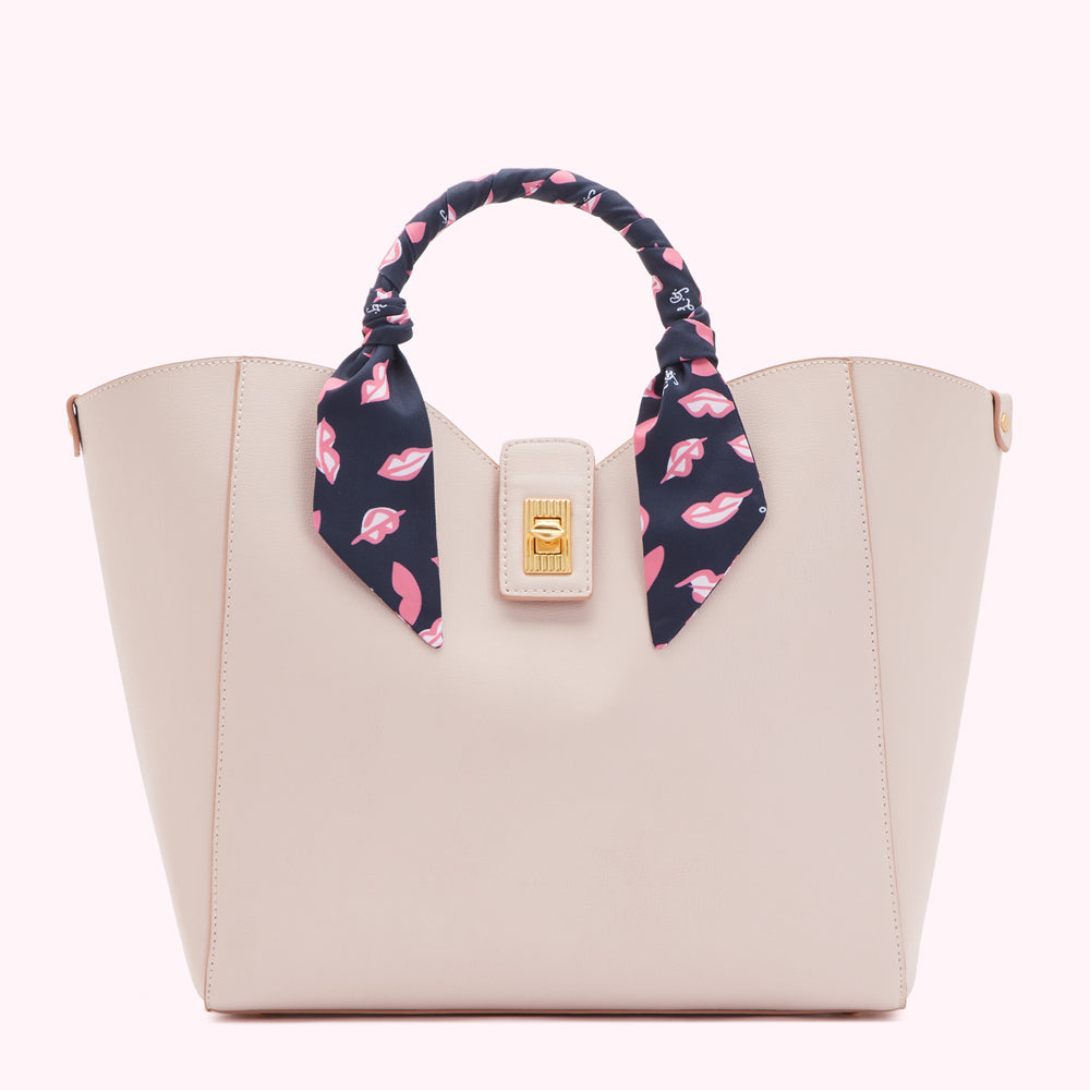 Beige tote bag with a navy blue and pink lips print scarf tied around the handles.