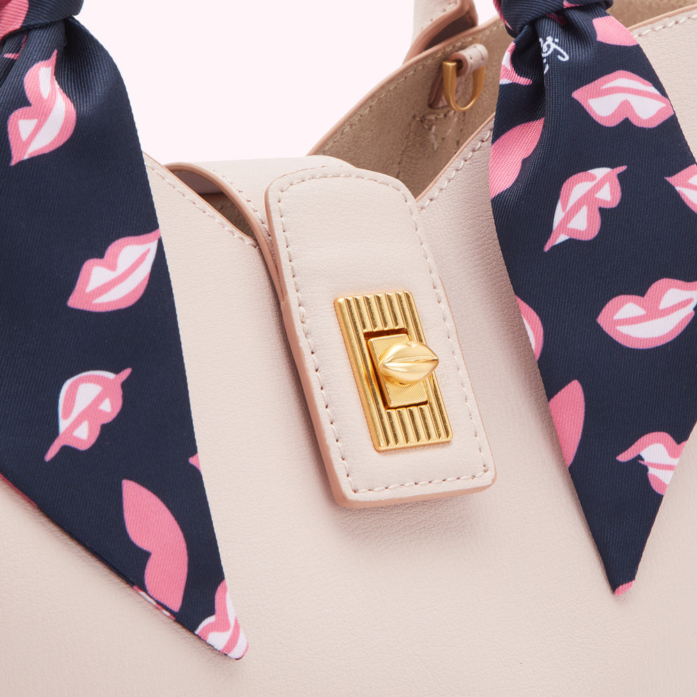 Close-up of a blush-colored leather handbag with a gold clasp and a navy blue scarf adorned with pink lips.
