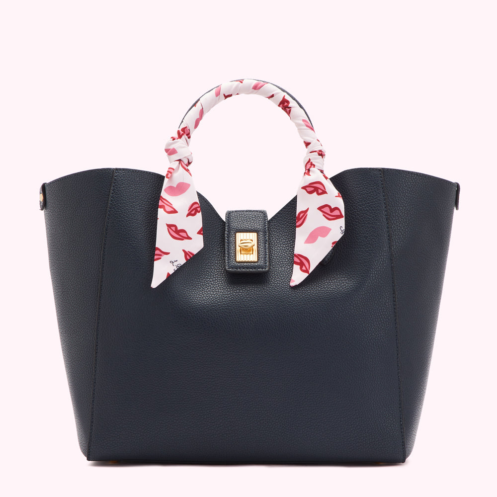Navy blue tote bag with a white silk scarf adorned with red lips printed on it around the handle.