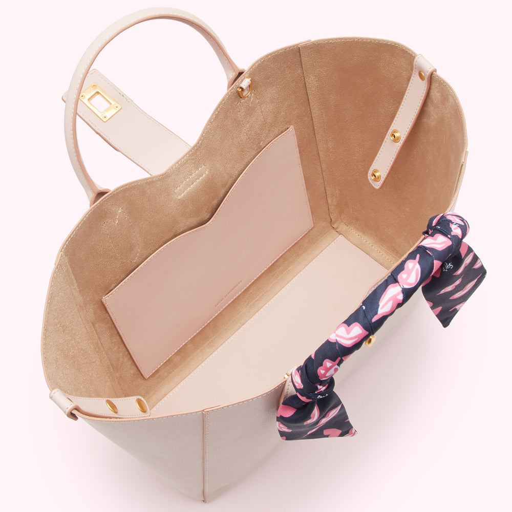 A light beige tote bag with a pink interior and a navy blue and pink scarf tied to the handle.