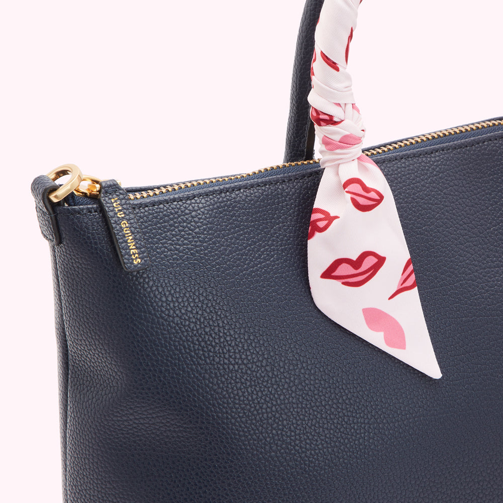 Close-up of a navy blue Lulu Guinness tote bag with a white silk scarf featuring red lips printed on it.