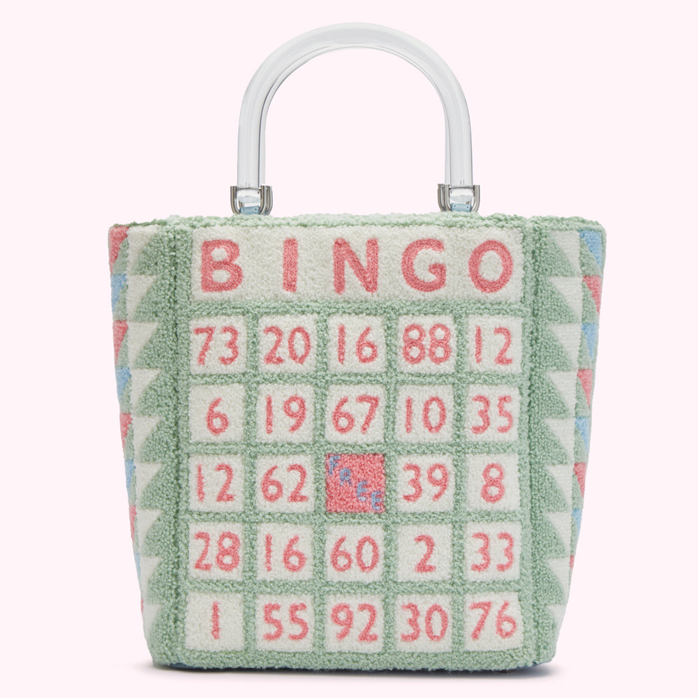 A pastel green tote bag with a clear handle features a bingo card design. The numbers are in pink, and the word "Bingo" is stitched at the top. The bag has a textured, possibly fuzzy, exterior.
