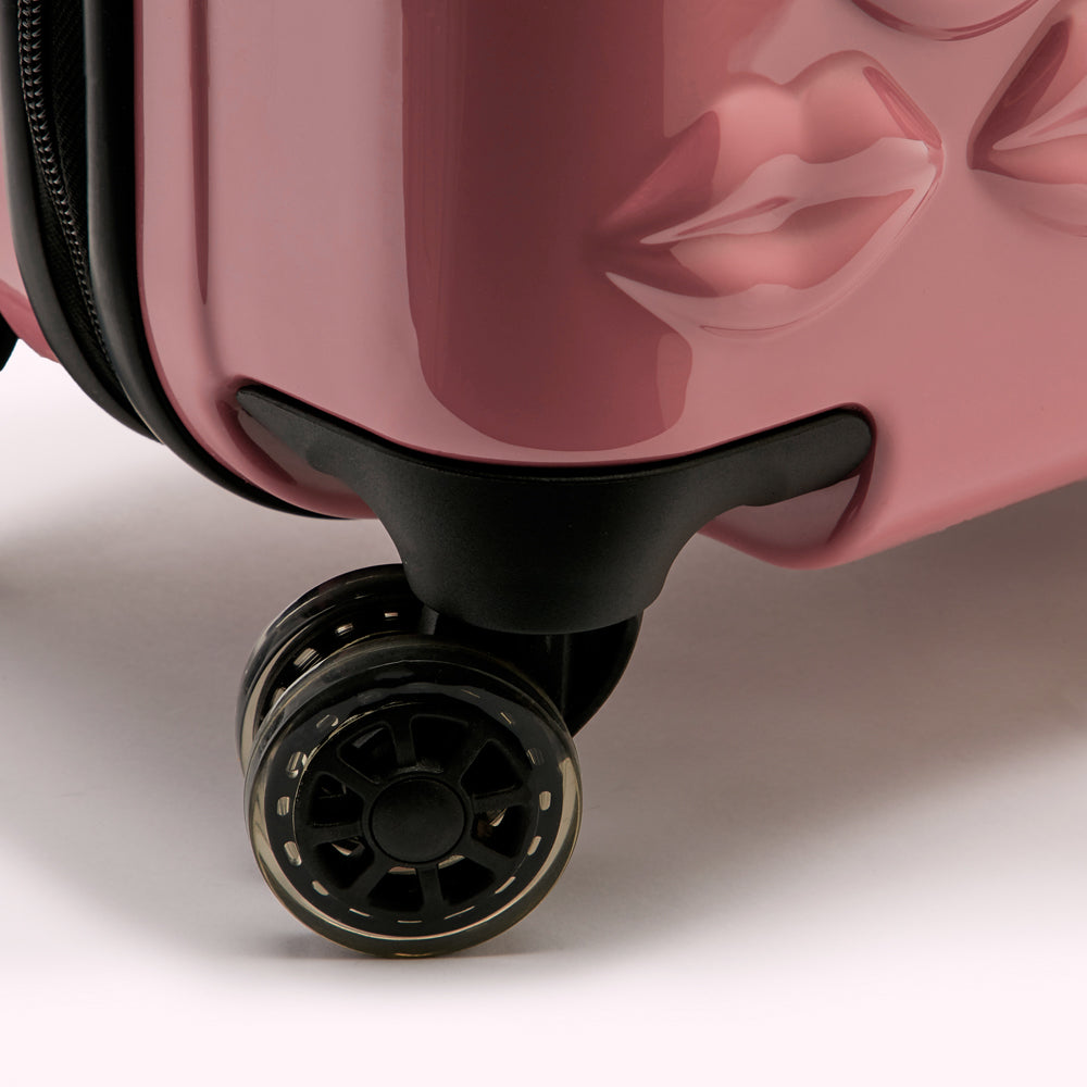 Close-up of the wheels and bottom of a pink carry-on suitcase with lips design.
