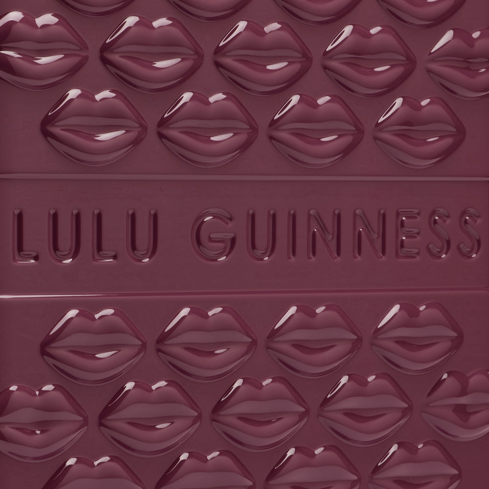 Close-up of a deep burgundy Lulu Guinness item featuring a repeating pattern of embossed lips and the brand name.
