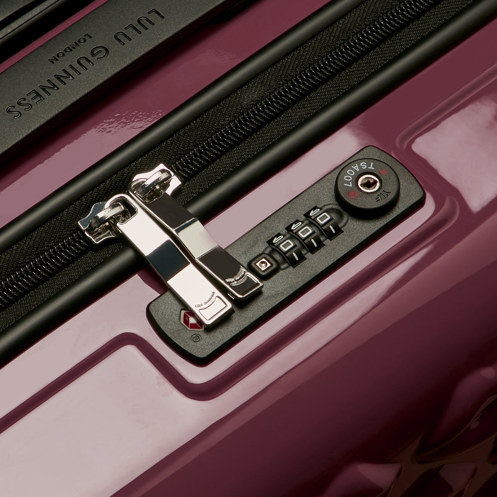 Close-up of a Lulu Guinness suitcase's TSA-approved combination lock and zipper pull. The suitcase is a deep mauve colour.
