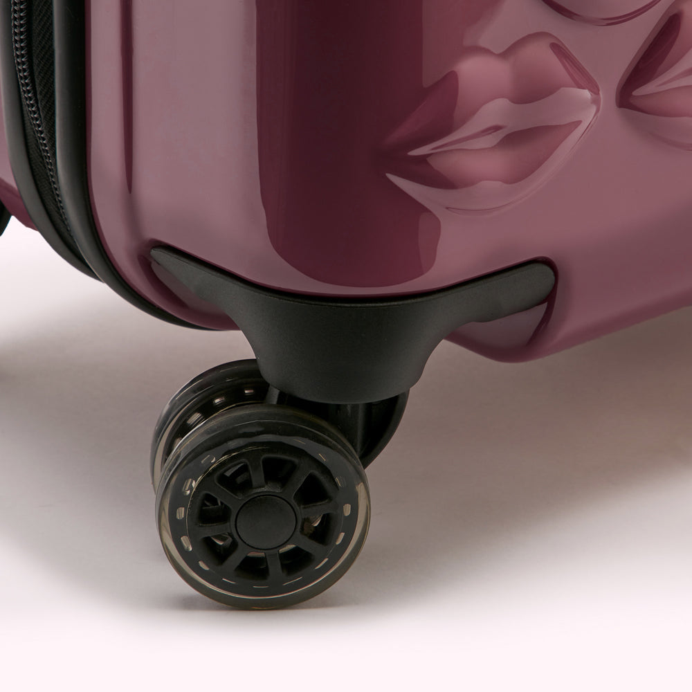 Close-up of a burgundy suitcase's wheels and base, featuring a unique lip design.
