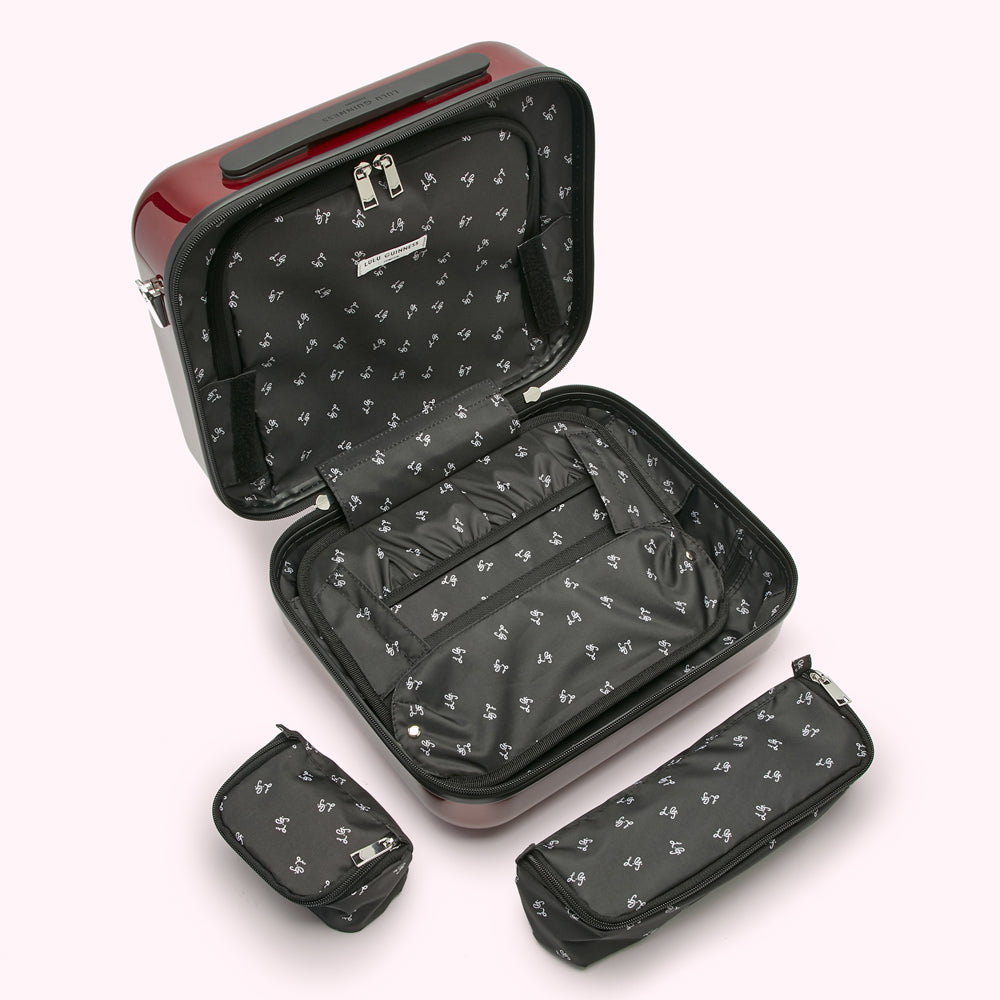 Red hard-shell carry-on suitcase open to reveal its black interior lining and various compartments; two additional matching zippered pouches are shown alongside.
